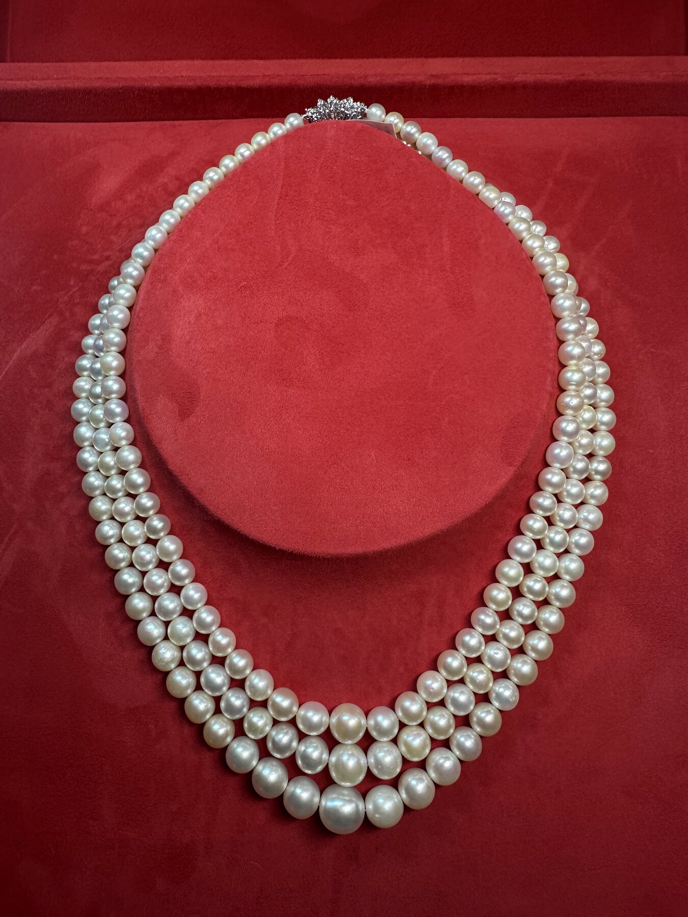 A graduated three-strand white natural pearl necklace with an elaborate diamond clasp, displayed on red suede.